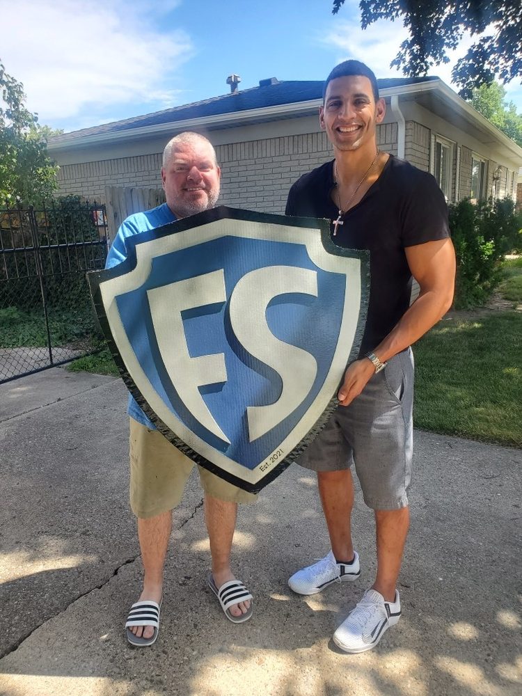 Custom Fit Society FS shield logo cutout in blue, silver and black, Est. 2021, held by two men outside