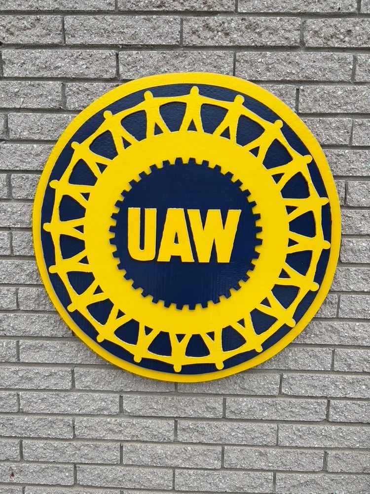 Custom UAW round gear logo cutout in yellow and navy mounted on a brick wall