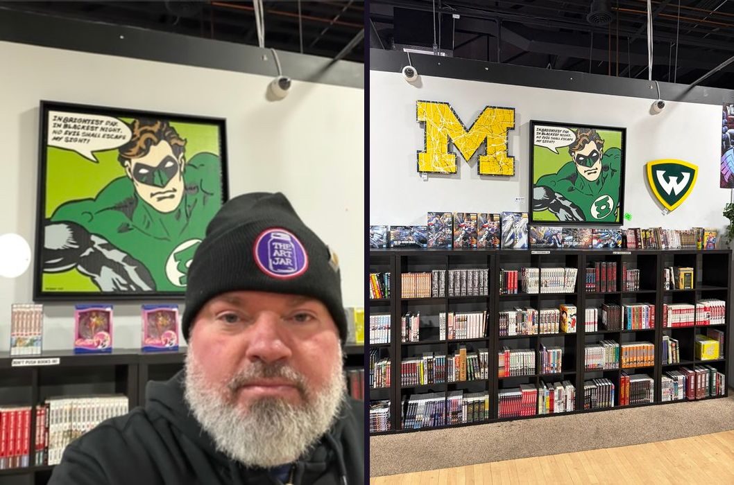 Comic and manga shop wall with a custom splatter-painted block M, a Wayne State W shield and a Green Lantern pop-art painting, plus the artist beside the painting
