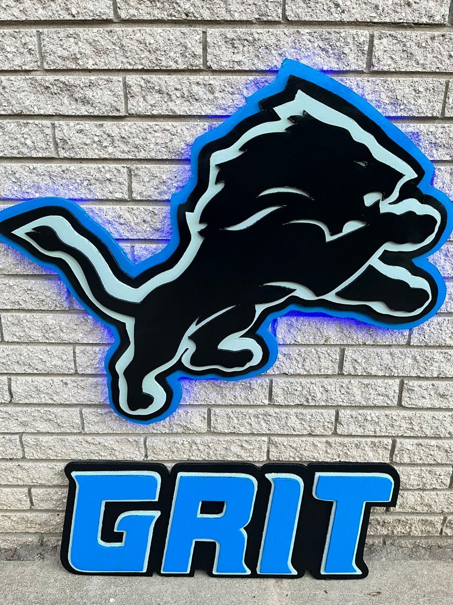 Custom black Detroit Lions logo cutout with blue LED glow and a GRIT sign on brick