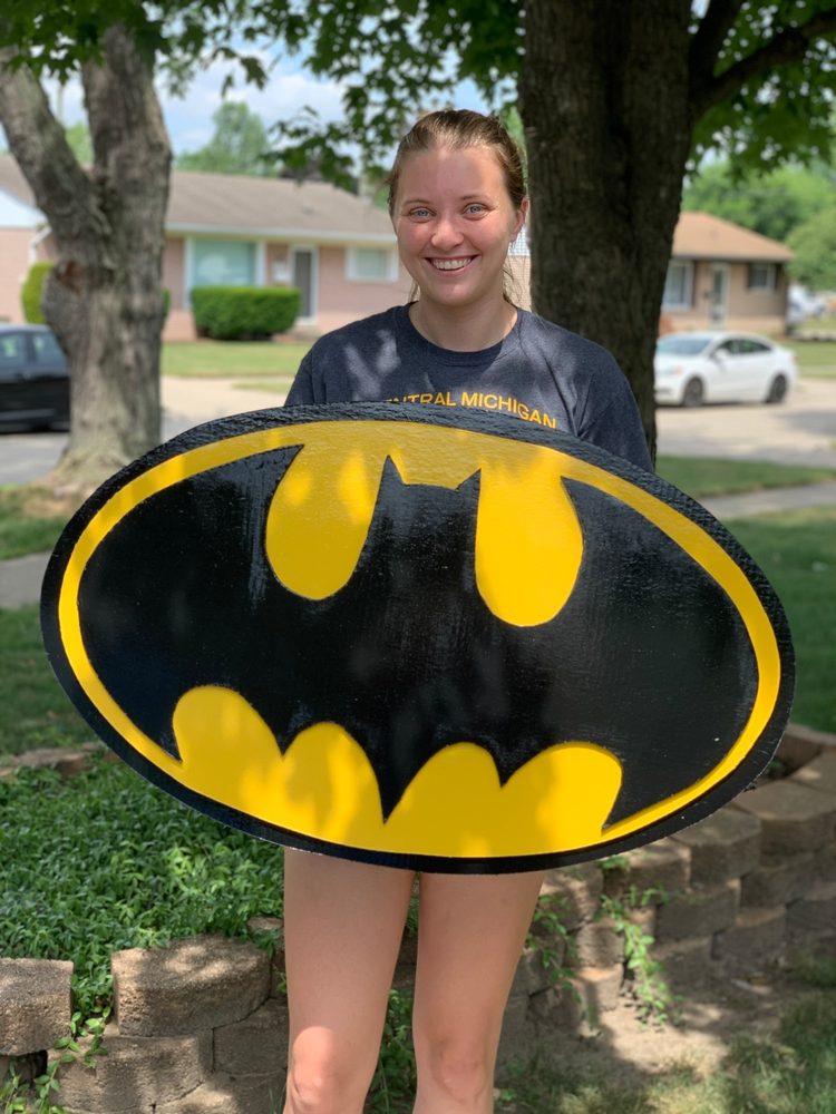 Custom Batman bat symbol oval cutout in black and yellow, held by a customer in a front yard