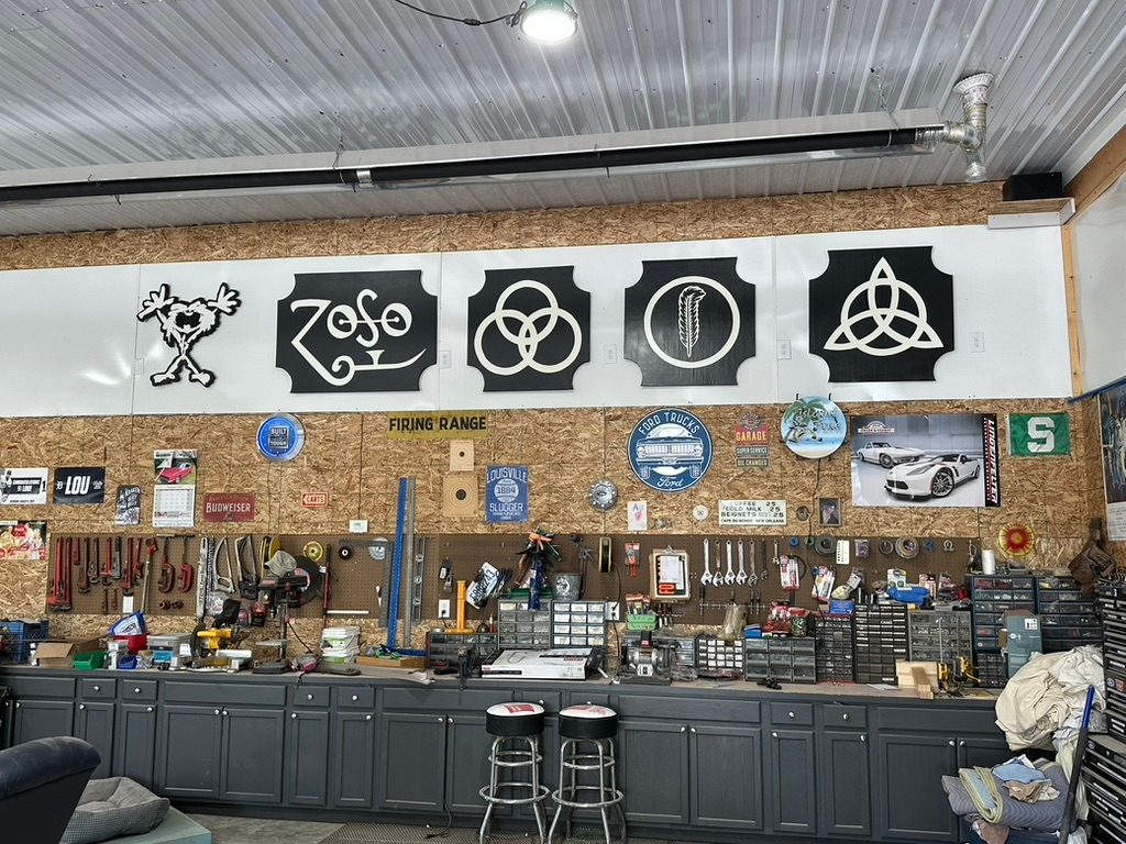 Custom Led Zeppelin symbol cutouts and a Pearl Jam stickman cutout on a garage wall: ZoSo, three rings, feather circle and triquetra