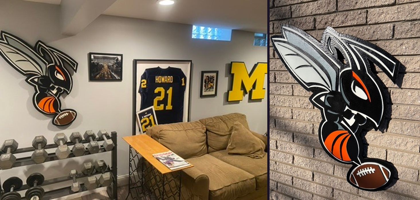 Custom hornet mascot cutout holding a football in black, orange and gray on a basement wall beside a framed Howard number 21 Michigan jersey and the maize Michigan M, and the hornet close up on brick