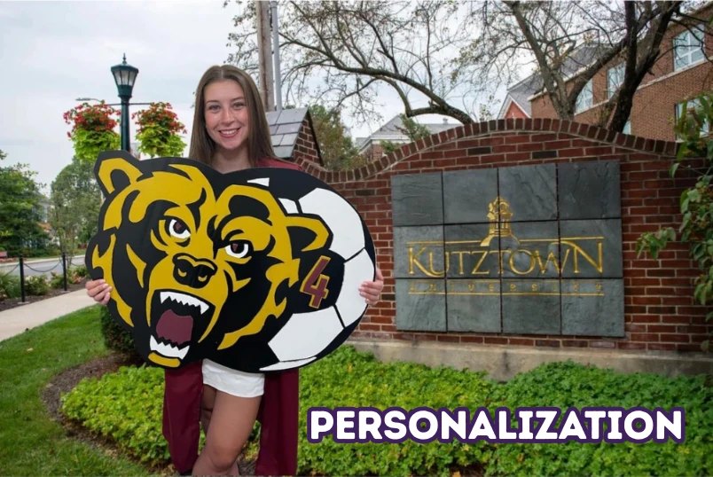 A Kutztown University student holding the custom Golden Bear and soccer ball number 4 cutout in front of the Kutztown University sign