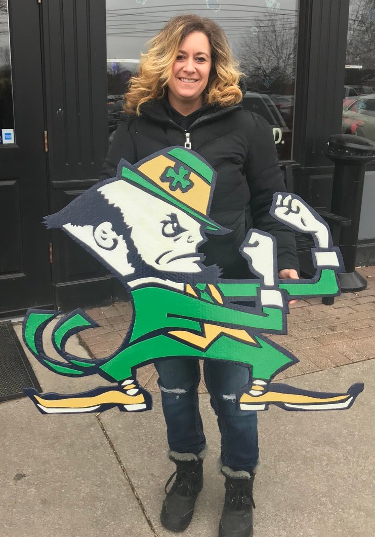 A customer holding the custom Notre Dame Fighting Irish Leprechaun cutout in green, gold and navy outside a storefront