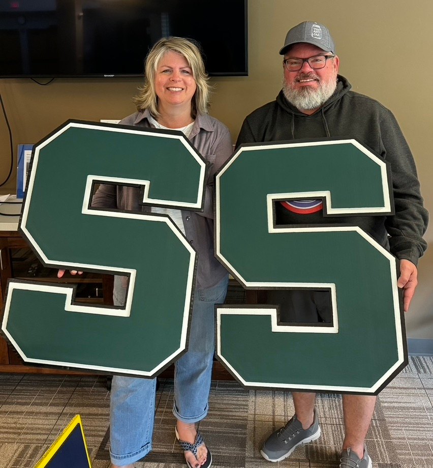 A couple holding two custom green Michigan State block S cutouts with white and black trim