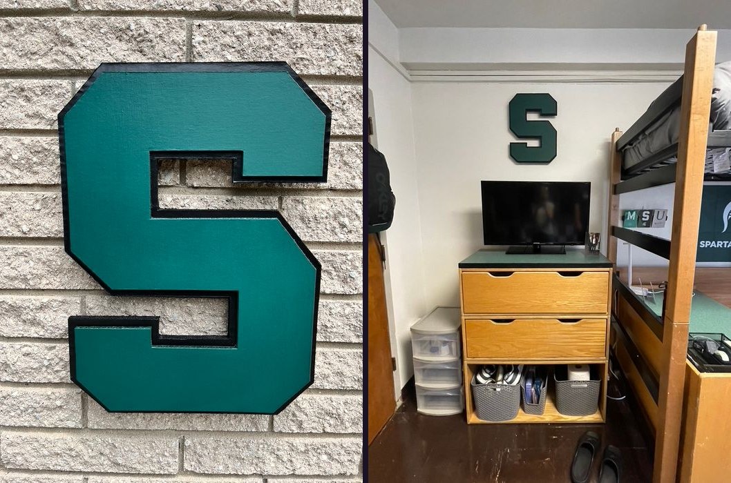 Custom green Michigan State block S cutout with black trim on a brick wall, and the block S hung above a TV in a dorm room