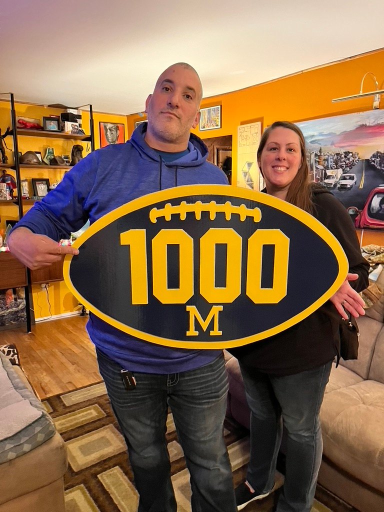 A couple holding the custom Michigan 1000 football cutout in their living room