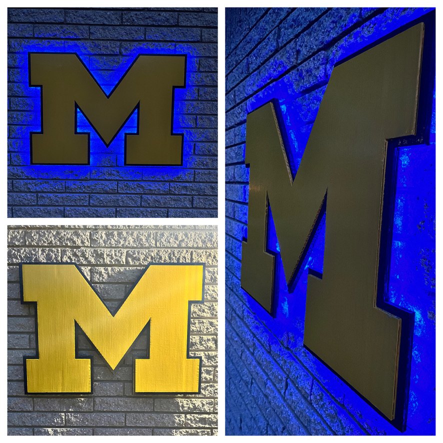 Custom Michigan block M cutout with blue LED backlighting on a brick wall at night, the same M in daylight, and an angled close-up