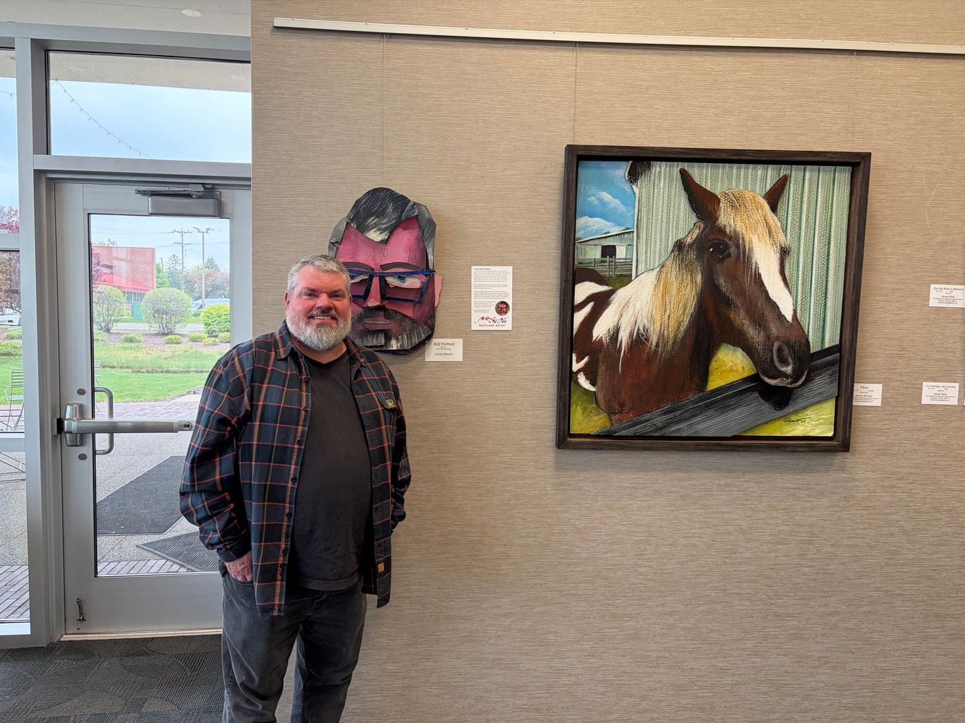 Jeremy Allen Rheault standing beside his Self Portrait and Finn on the gallery wall
