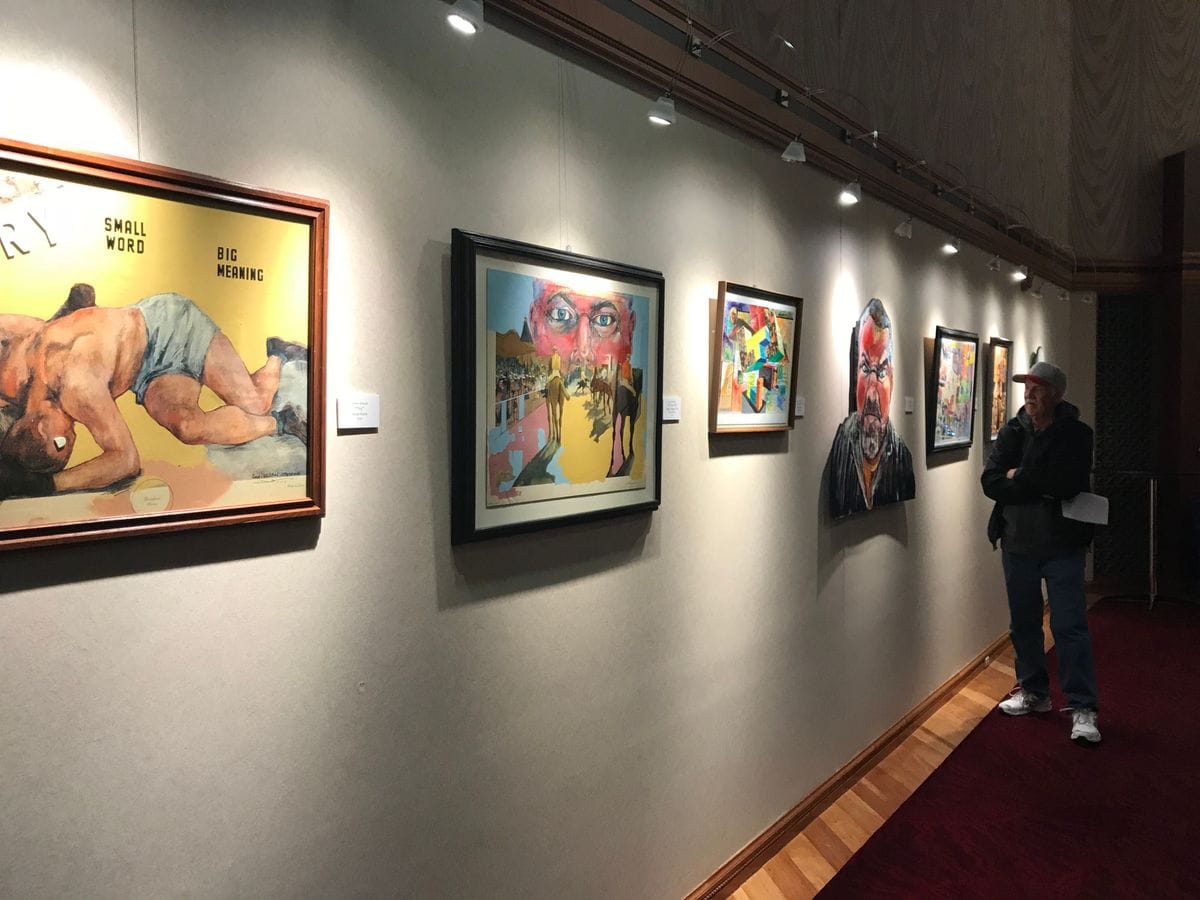 Framed mixed media works along the hallway with a visitor looking