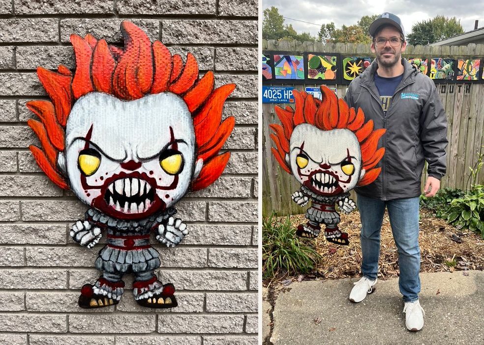 Hand-cut and hand-painted Funko Pop style Pennywise with orange hair, yellow eyes and sharp teeth: on a brick wall, and held by the customer in a backyard