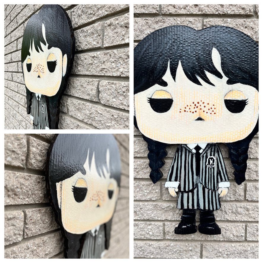 Hand-cut and hand-painted Funko Pop style Wednesday Addams with braids, freckles and a striped Nevermore uniform: front view on a brick wall and two angled close-ups showing the layered depth