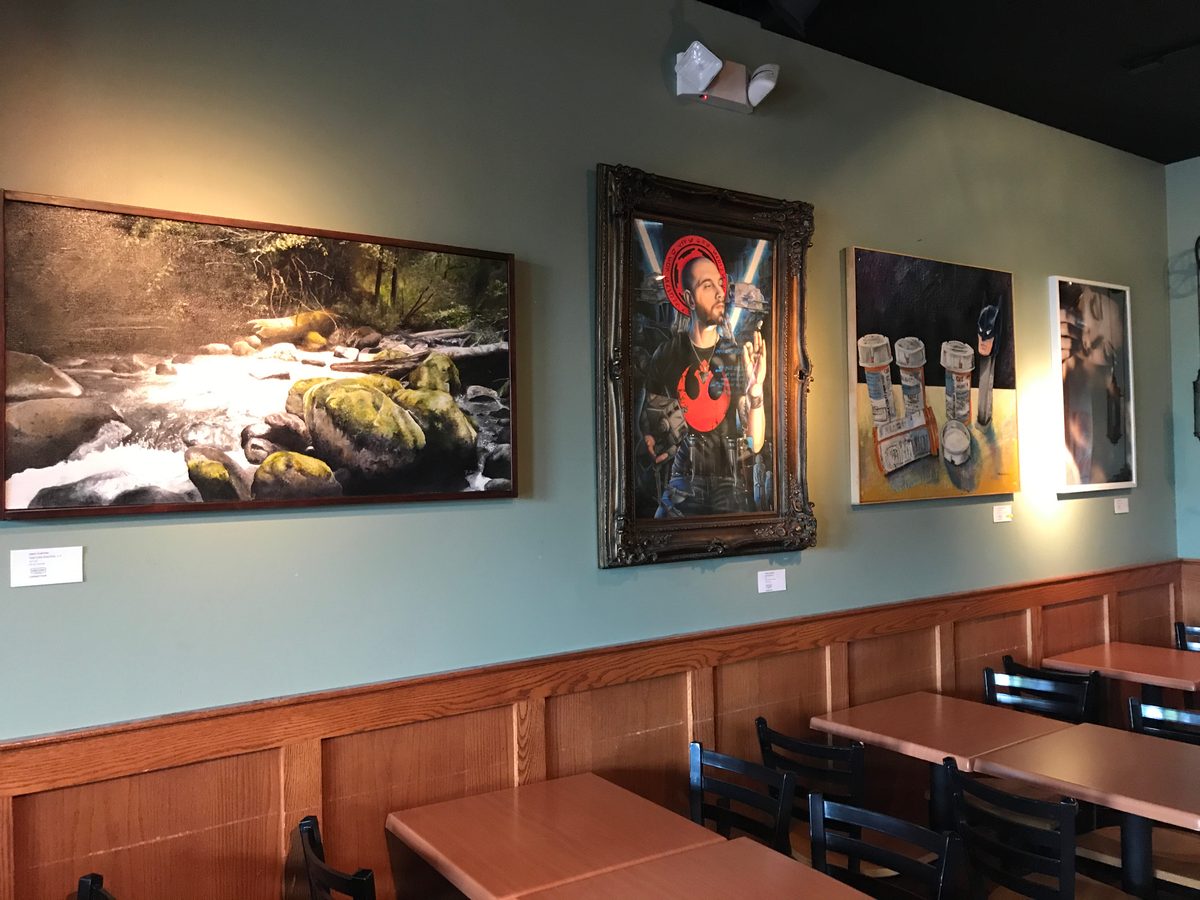 Framed river landscape, an ornate-framed portrait and other pieces hung on the sage-green wall above the wood wainscoting