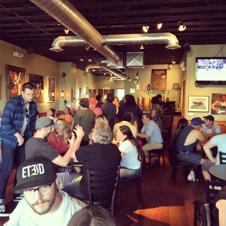 A crowded Liberty Room Gallery during the Connection opening, with framed art on the walls above the guests