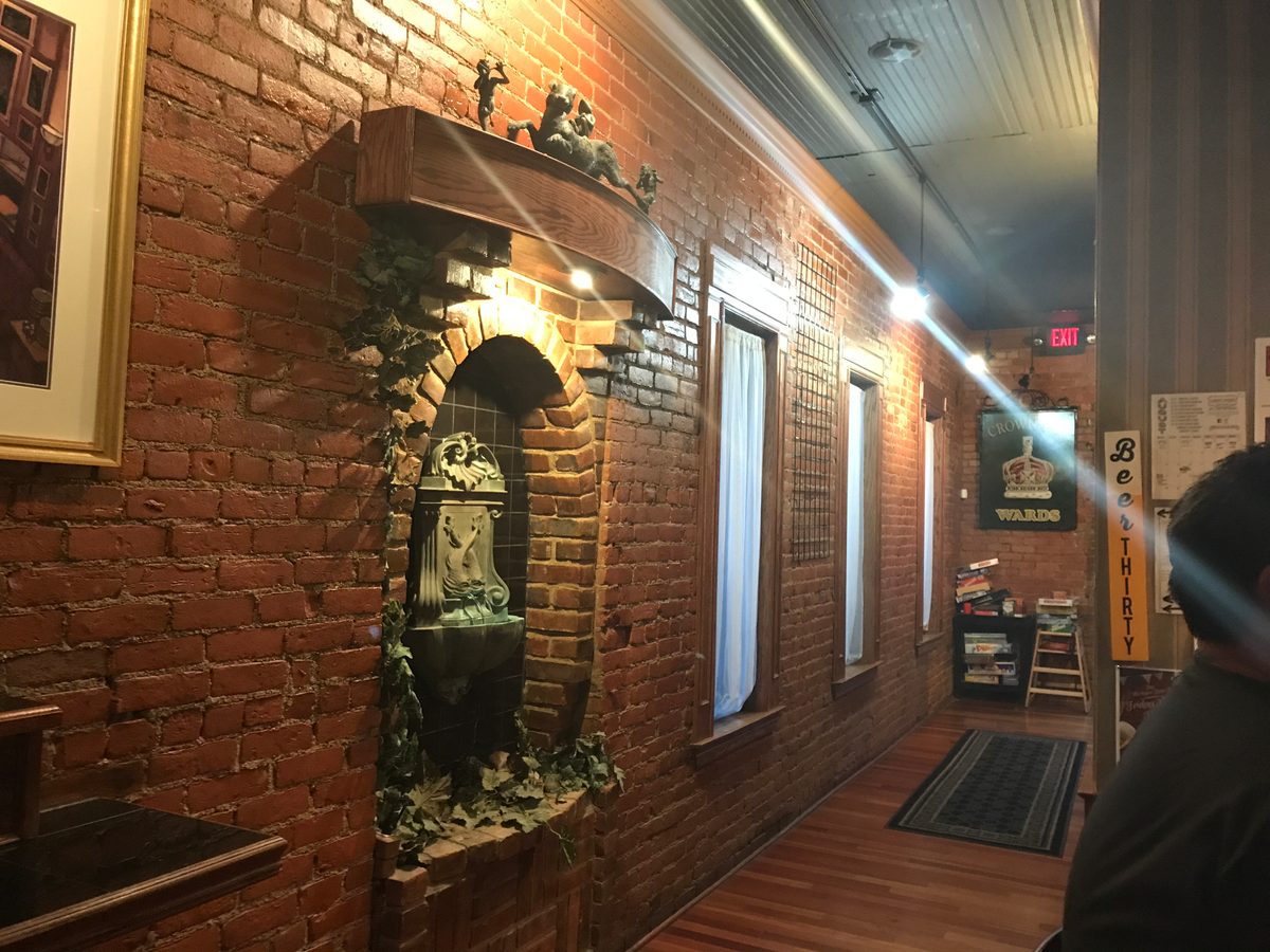 Brick wall with a lit fountain niche and framed pieces along the hallway of the gallery