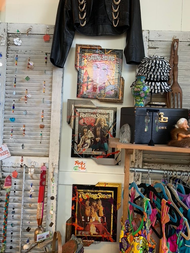 Three hand-embellished Rolling Stone cover pieces in splatter-painted frames hung on a white wall at Finders Keepers, between a leather jacket above and a clothing rack and shelf beside them