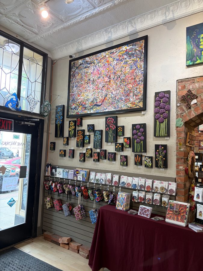 Persevere, a large multicolor splatter painting in a black frame, on the wall at Frame Works above small floral paintings and the front door