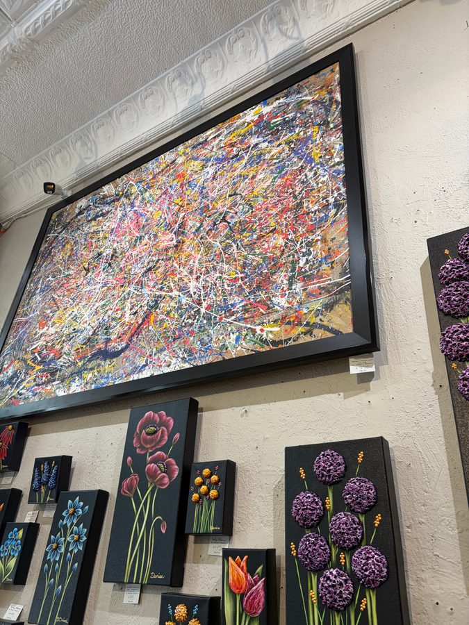 Angled view of Persevere in its black frame, with small black floral paintings below it