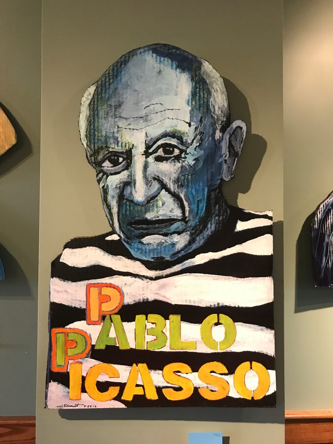 Hand-cut and hand-painted Pablo Picasso portrait in a striped shirt lettered PABLO PICASSO, hanging on the wall at Liberty Street Brewing Company