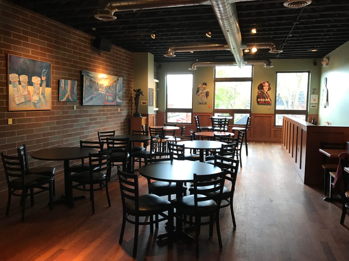Wide view of the Up Stairs Hall at Liberty Street Brewing Company with paintings hung along the brick wall and tables set below