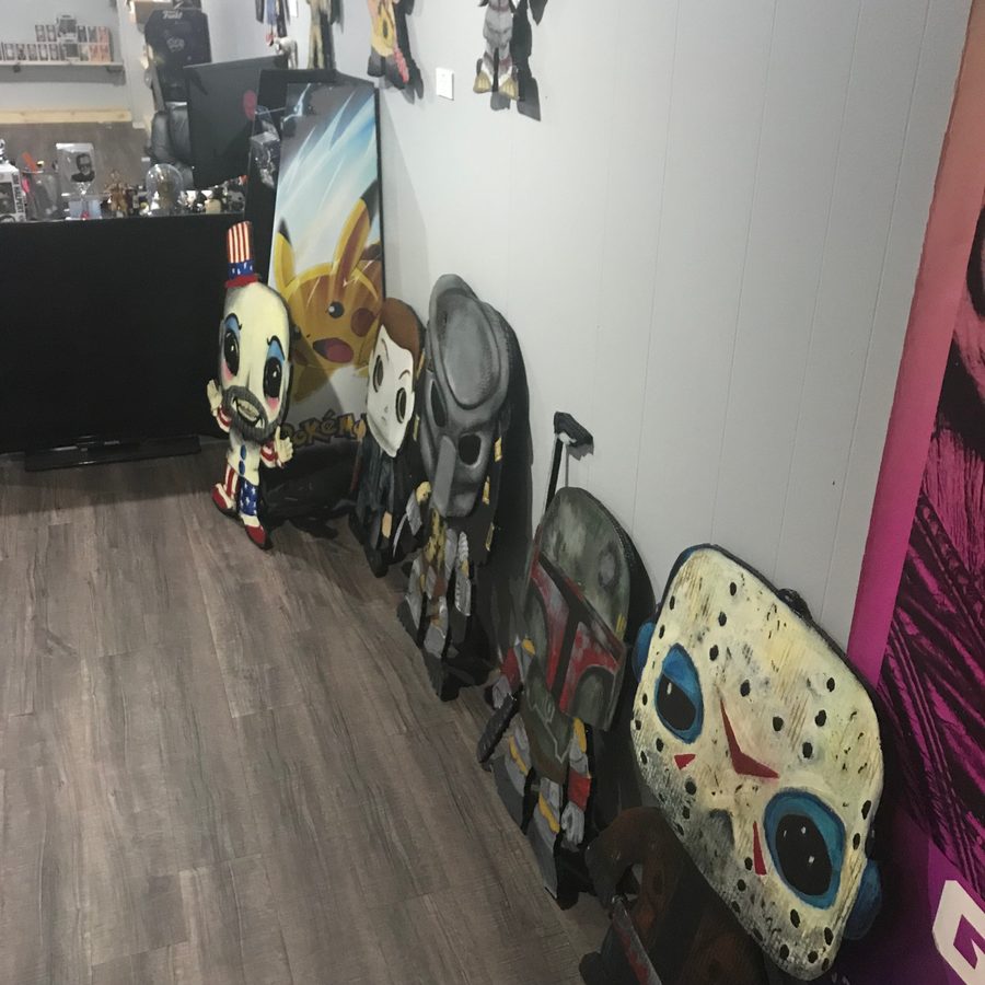 Panoramic view of Funko-style cutouts lined up along a white wall at Popgodz, including Captain Spaulding, Predator, Boba Fett and Jason