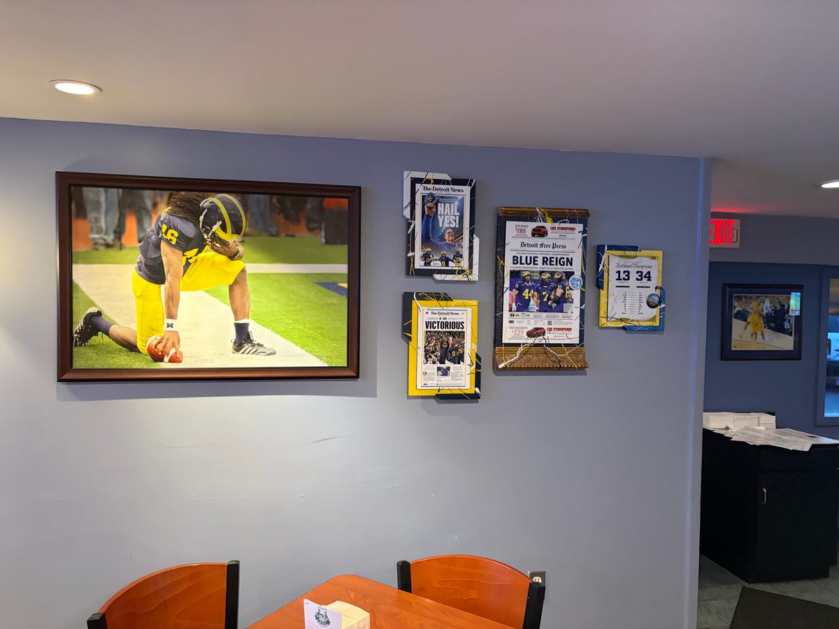 Framed Michigan football front pages and a 13-34 ticket piece beside a large framed photo