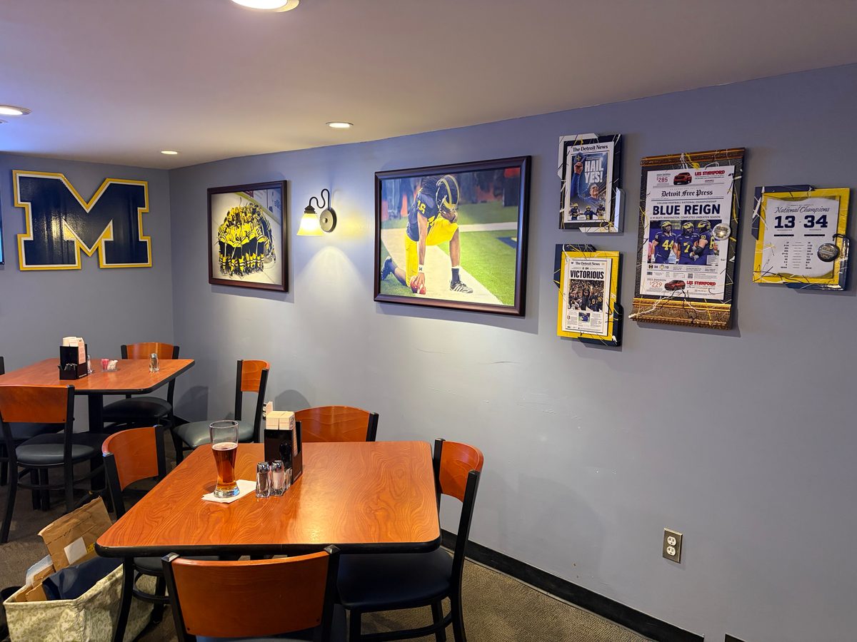 Wall of framed Michigan football newspapers, tickets and photos in yellow frames next to a Michigan M