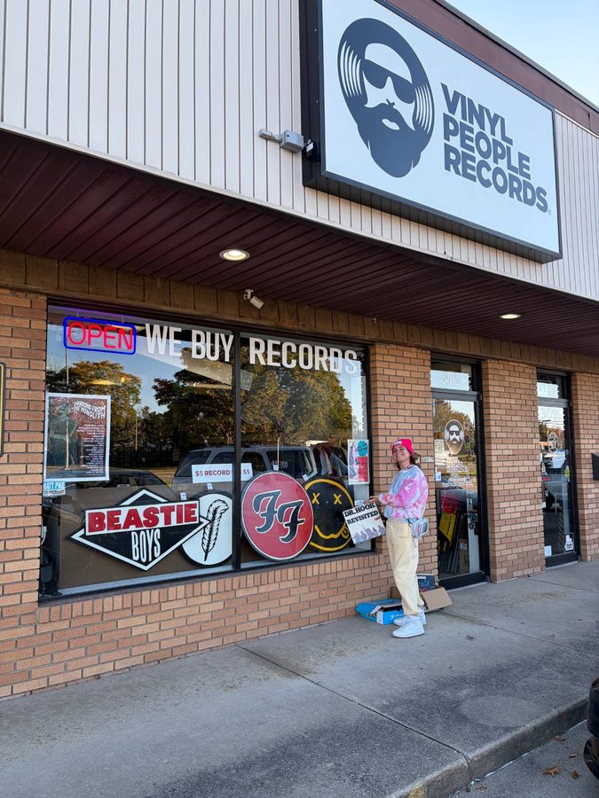 A customer in a pink beanie holding a record outside Vinyl People Records, with the hand-cut Beastie Boys, Led Zeppelin, Foo Fighters and Nirvana logos in the front window