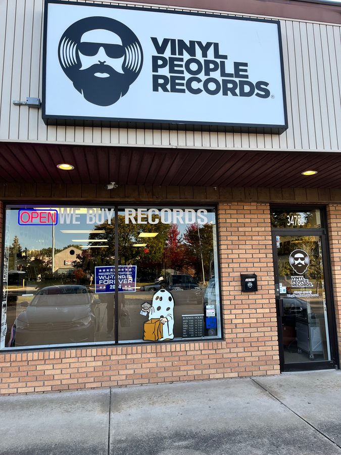 Storefront of Vinyl People Records in Westland with the bearded record logo sign and a We Buy Records window