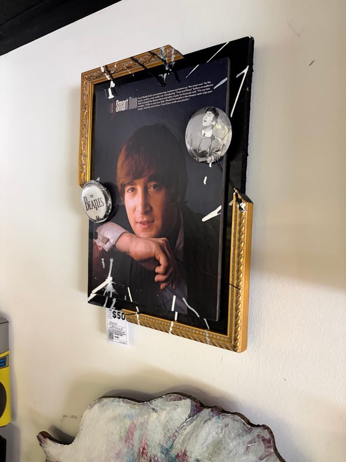 Framed John Lennon portrait piece with paint splatter and Beatles buttons in a gold frame, hanging on the wall at Vinyl People Records