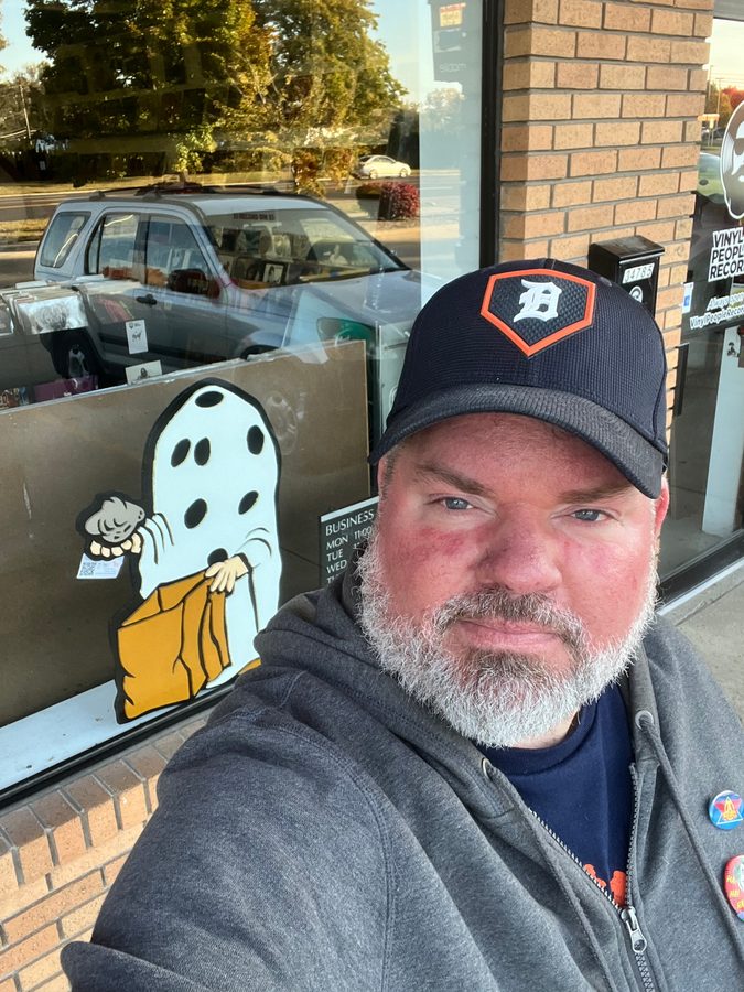 Jeremy Rheault taking a selfie in a Tigers cap outside the Vinyl People Records window with a ghost graphic