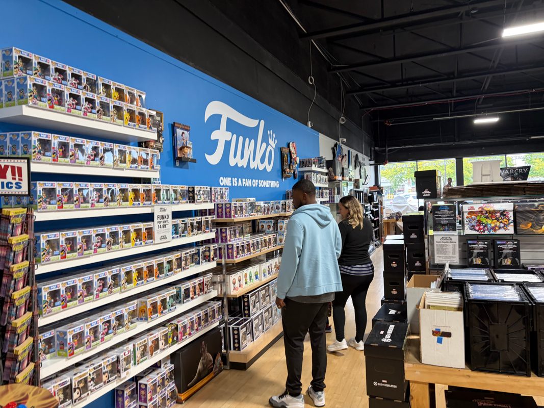 Customers browsing the Funko wall at State of Comics with the logo cutouts in the distance