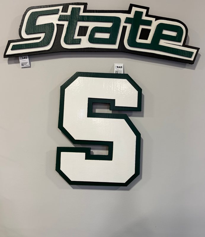 Hand-cut State wordmark and Spartan S logo cutouts on a gray wall