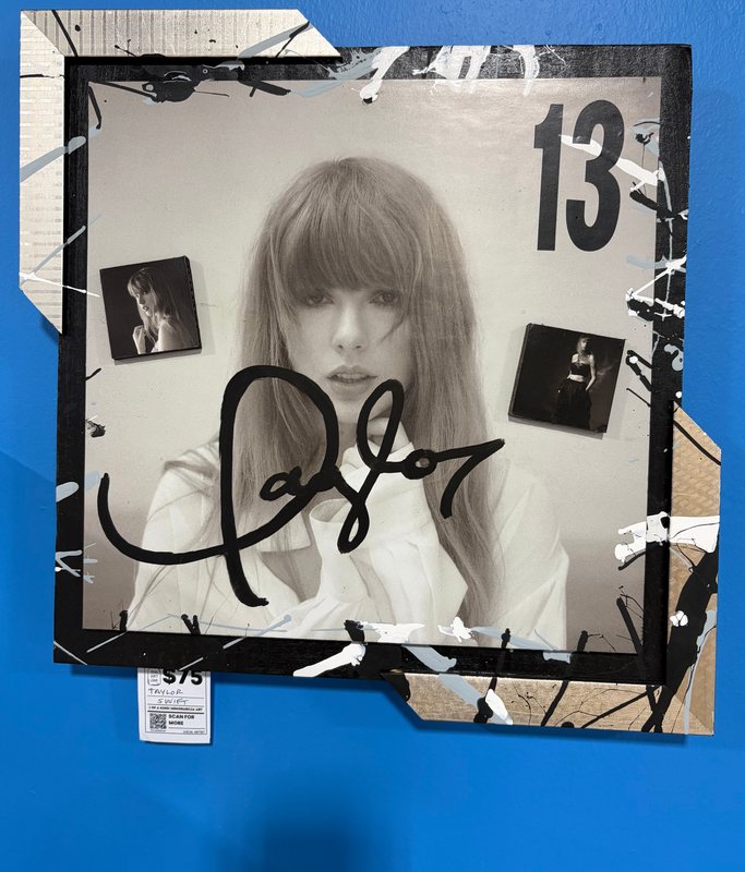 Hand-embellished Taylor Swift album art with a signature and splatter paint on a blue wall